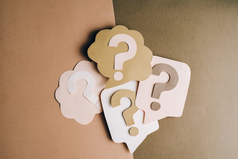 A collection of five paper cutouts featuring question marks, arranged on a two-tone background with the left side in light brown and the right side in darker beige. The question marks are in neutral t